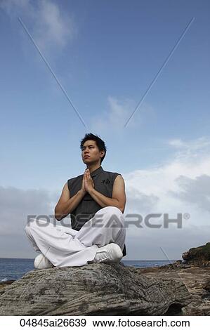 Stock Photo - Chinese man doing yoga on rock. Fotosearch