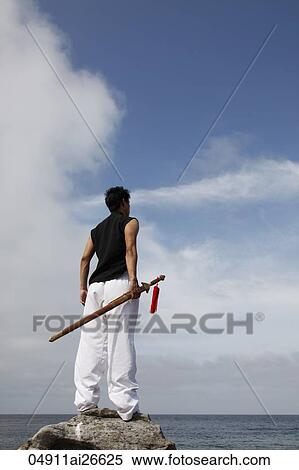 Stock Photography - Chinese man holding a sword looking at ocean.. Fotosearch