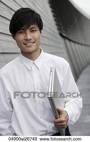 Chinese man holding lap top in front of building View Large Photo Image Stock Photo - Chinese man holding lap top in front of building. Fotosearch