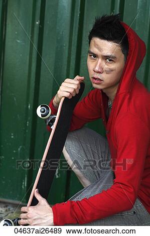 Stock Photo - Chinese man holding skateboard with dirt on his face. Fotosearch