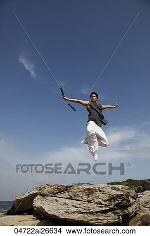 Picture - Chinese man jumping in air holding nunchucks. Fotosearch