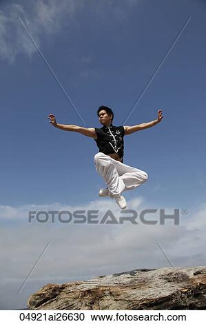 Stock Image - Chinese man jumping in air while doing a martial arts pose. Fotosearch