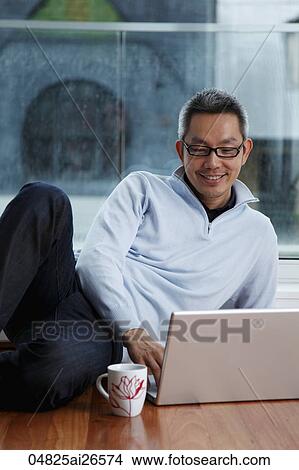 Chinese man sitting near window looking at lap top View Large Photo Image Picture - Chinese man sitting near window looking at lap top. Fotosearch