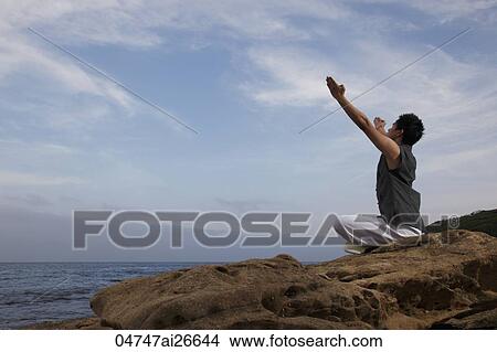 Chinese man sitting on rock raising his arms to the sky View Large Photo Image Picture - Chinese man sitting on rock raising his arms to the sky. Fotosearch