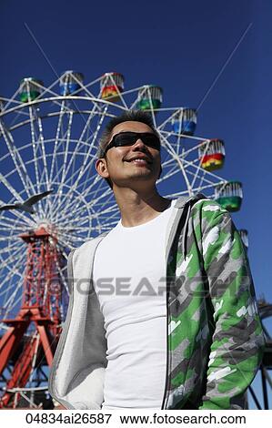 Stock Photo - Chinese man smiling in front of ferris wheel. Fotosearch