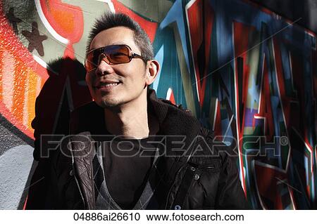 Stock Image - Chinese man smiling next to wall with graffiti. Fotosearch