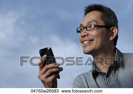 Stock Image - Chinese man smiling while reading text on phone. Fotosearch