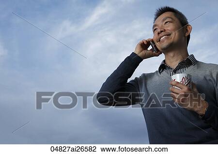 Stock Image - Chinese man talking on phone and smiling outside. Fotosearch