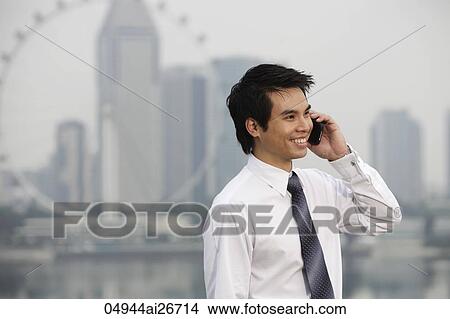 Picture - Chinese man talking on phone in front of city sky line. Fotosearch