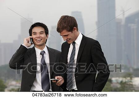 Stock Photo - Chinese man talking on phone while Caucasian man texts.. Fotosearch