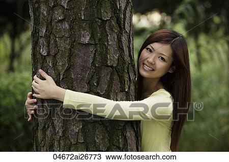 Stock Image - Chinese woman hugging a tree and smiling. Fotosearch