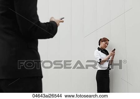 Close up of man using hand phone while woman reads text in back ground. View Large Photo Image Picture - Close up of man using hand phone while woman reads text in back ground.. Fotosearch