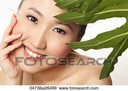 Stock Photo - Head shot of Chinese woman smiling with green leaf. Fotosearch