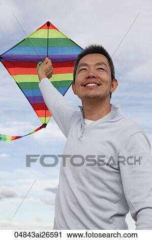 Stock Image - Man flying colourful kite and smiling. Fotosearch