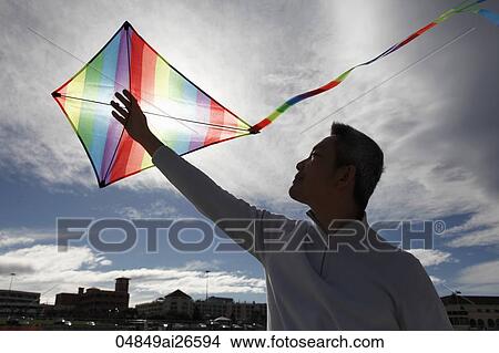 Man holding kite up in the air as sun shines through View Large Photo Image Picture - Man holding kite up in the air as sun shines through. Fotosearch