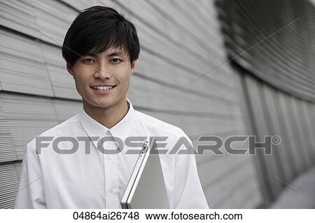 Stock Photo - man holding lap top next to a building. Fotosearch