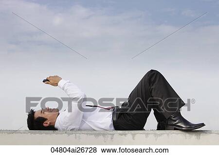 Stock Photo - man in suit laying on ground looking at phone, smiling. Fotosearch