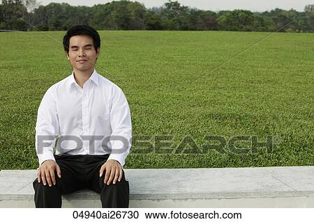 Man in white shirt sitting on grass with eyes close View Large Photo Image Stock Image - Man in white shirt sitting on grass with eyes close. Fotosearch