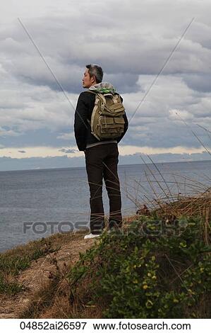 man wearing a back pack standing on trail overlooking the ocean View Large Photo Image Stock Photo - man wearing a back pack standing on trail overlooking the ocean. Fotosearch