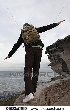 Man wearing back pack balancing on wall with a view of the ocean View Large Photo Image Stock Image - Man wearing back pack balancing on wall with a view of the ocean. Fotosearch