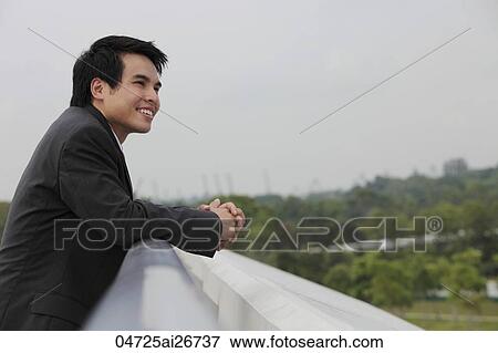 Stock Photo - Man wearing suit leaning on wall and looking at view. Fotosearch