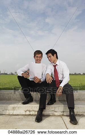 Two business men sitting outside looking at piece of paper View Large Photo Image Stock Photograph - Two business men sitting outside looking at piece of paper. Fotosearch