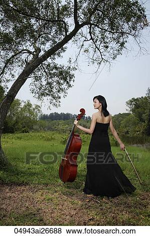 Stock Photo - Woman holding cello outside under a tree. Fotosearch