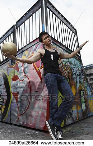 Picture - Young man holding basket ball in front of graffiti wall. Fotosearch