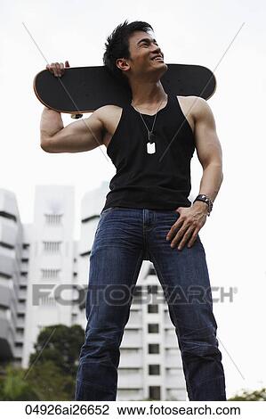 Stock Image - Young man holding skateboard on his shoulders. Fotosearch