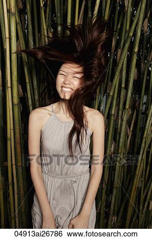 Stock Photograph - Young woman flipping her hair in front of bamboo. Fotosearch