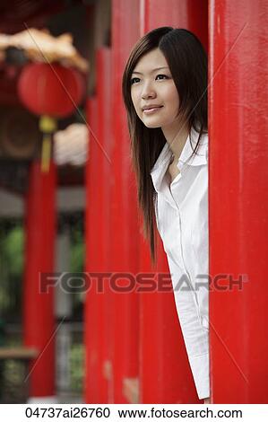 Stock Image - Young woman looking out from behind red pillars. Fotosearch
