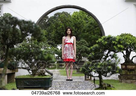 Stock Photo - Young woman standing with bonsai trees. Fotosearch