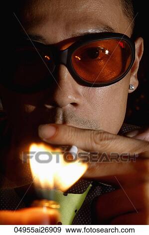 Stock Photo - close up of man lighting cigarette while wearing sunglasses. Fotosearch