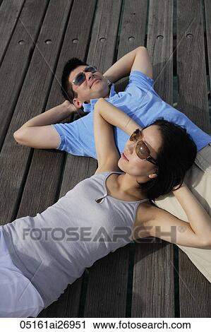 Stock Image - couple lying on backs on wooden floor, wearing sunglasses. Fotosearch