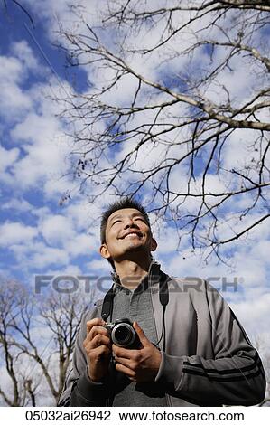 Stock Image - man holding camera looking up to sky. Fotosearch