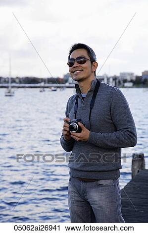 man holding camera near water and smiling View Large Photo Image Stock Image - man holding camera near water and smiling. Fotosearch
