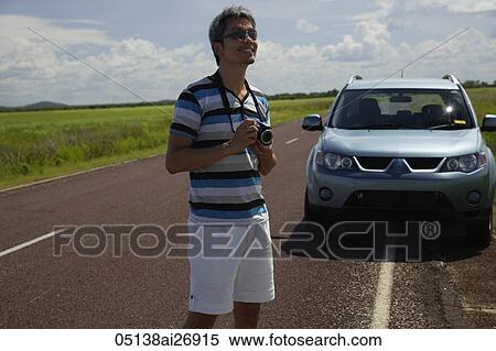 man holding camera next to road, car in background View Large Photo Image Stock Photography - man holding camera next to road, car in background. Fotosearch