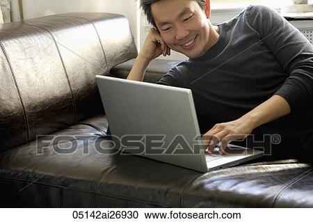 Stock Image - man laying on sofa with lap top. Fotosearch