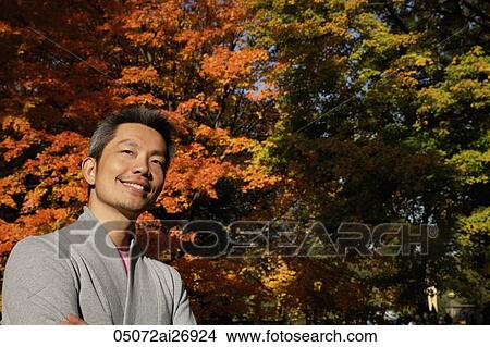 Picture - man looking up and smiling with trees changing colors in background. Fotosearch