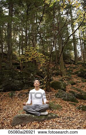 Stock Image - man sitting in forest meditating. Fotosearch