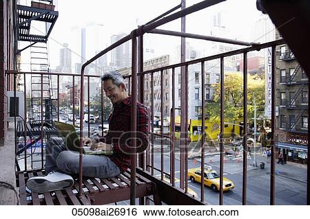 Stock Photograph - man sitting on fire escape working on lap top. Fotosearch