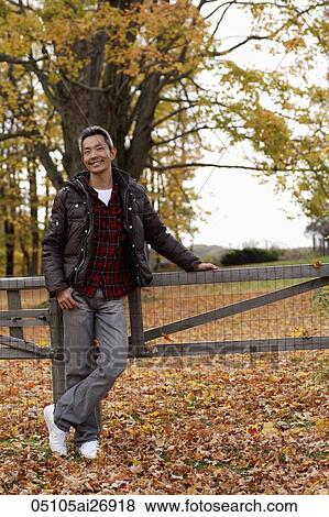 Stock Photo - man standing next to fence with fallen leaves on the ground. Fotosearch