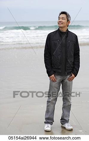 Picture - man standing on beach wearing a coat and smiling. Fotosearch
