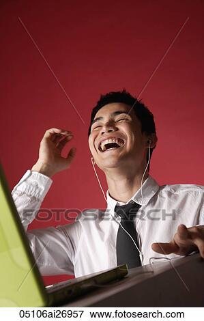 Stock Photo - man wearing ear phones looking at lap top and laughing. Fotosearch