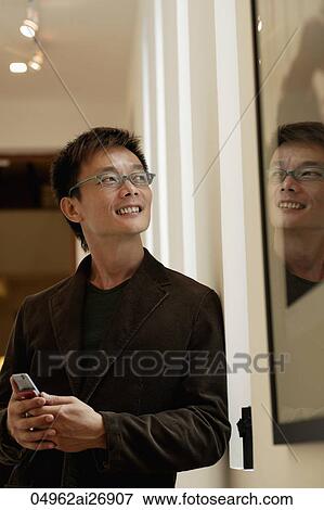 Man wearing glasses looking out window holding phone View Large Photo Image Stock Photo - Man wearing glasses looking out window holding phone. Fotosearch