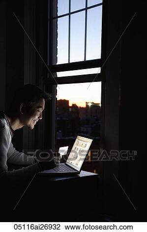 Stock Image - profile of man working on laptop in evening. Fotosearch