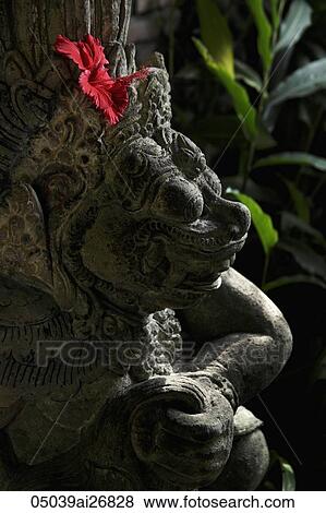 Stock Photo - red hibiscus in stone Hindu statue. Fotosearch