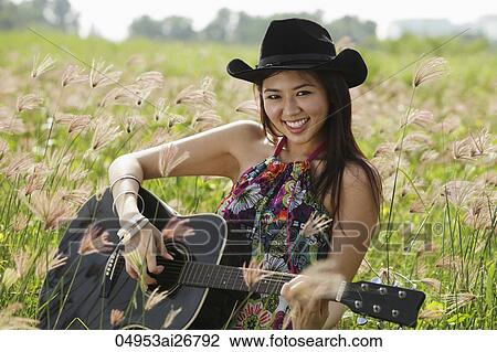 Stock Image - smiling woman playing guitar in grassy field. Fotosearch