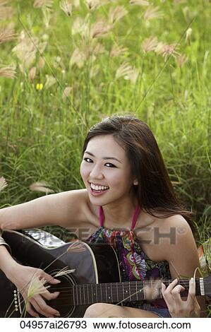 Stock Image - smiling woman playing guitar on grass. Fotosearch