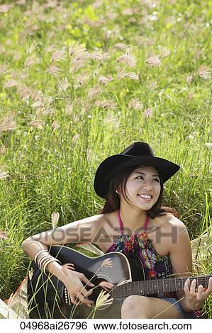 Stock Photograph - smiling woman playing guitar outside on the grass. Fotosearch